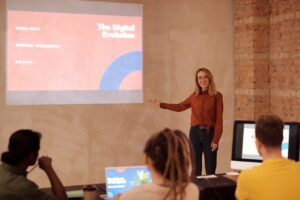 Professora apresenta tema sobre inteligência artificial e evolução digital para estudantes universitários em sala de aula, destacando o impacto da IA na educação.